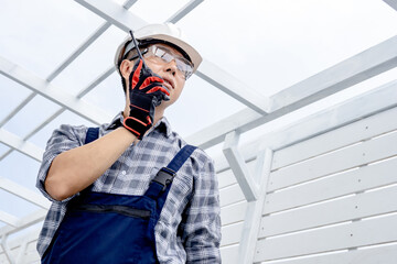 Confident Asian man civil engineer looking forward and talking on walkie talkie. Smart male foreman...