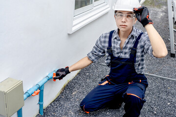 Asian male plumber in protective workwear looking at the camera while checking valve on water pipe...