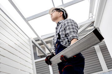 Roof installation process. Asian man roofer in protective workwear installing steel beam at building site. Male construction worker holding metal part of roof structure. House extension and renovation