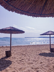 Beach, straw umbrellas, sea, empty sky and island in the distance