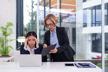Asian Women Feeling Stressed at Work with Older Asian Manager Reviewing Documents for Business...