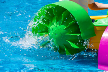 green paddle wheel on a children's boat splashing water in a pool. A dynamic scene of summer...