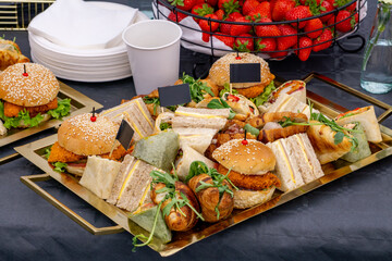Tray with a variety of catering snacks – burgers, wraps, mini sandwiches, and croissants,...