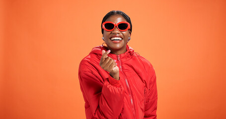 Heart, fashion and portrait of woman in studio for love, support and trendy style on orange background. Happy, smile and person with emoji, gesture and fingers for gratitude, thank you and confidence