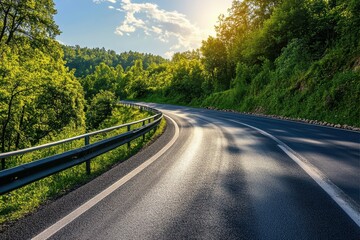 Fototapeta premium Winding highway through lush greenery under a bright sky with sunlight shining on the road and crash barriers alongside