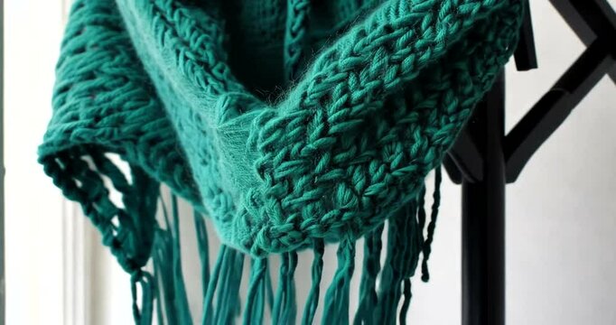A close-up view of a beautifully knitted teal scarf draped elegantly on a wooden stand, showcasing intricate patterns