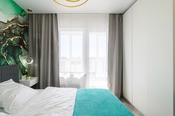 modern bedroom with a green accent wall, white bedding and turquoise throw, gray curtains, a white...