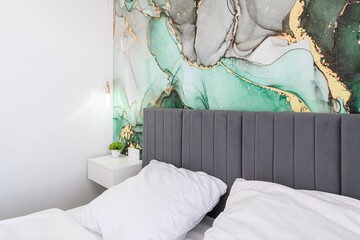 Bedroom featuring a grey headboard, white bedding, bedside table, a modern wallpaper, and hanging...