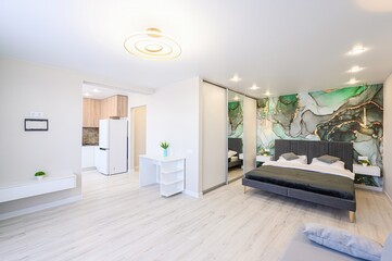 Bright studio apartment with a modern interior design, featuring a kitchen area, bedroom space with a green marble accent wall, and sleek white furniture