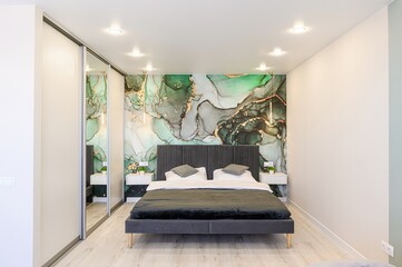stylish bedroom features a gray bed against a green and gold marbled accent wall. Mirrored closet...