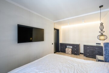 Bright bedroom with TV on the wall, white bed, vanity table, and a modern lamp