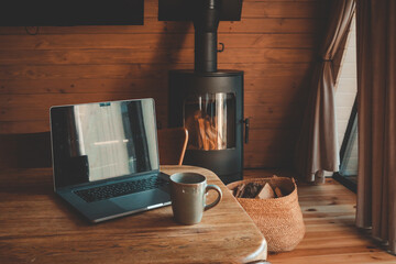 Laptop and coffee mug on a wooden table in cozy cabin interior, sunlight streaming through window, peaceful remote workspace setup