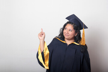 Young brunette Latina woman wearing a cap and gown celebrates her graduation and the completion of...