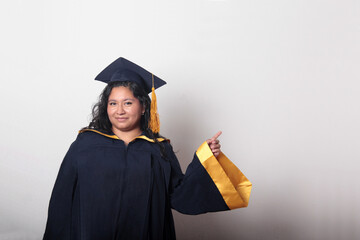 Young brunette Latina woman wearing a cap and gown celebrates her graduation and the completion of...