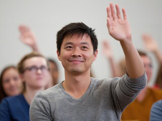 Smiling Asian man in 20s raising hand in a meeting with diverse people
