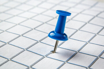 Bright blue pushpin, firmly inserted into a white graph paper, representing a key point or location