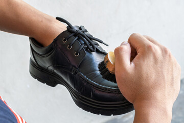 Close-up of hands wiping and polishing black leather shoes using a cloth. Shoe cleaning, leather care, daily hygiene routine, personal grooming, isolated on plain background