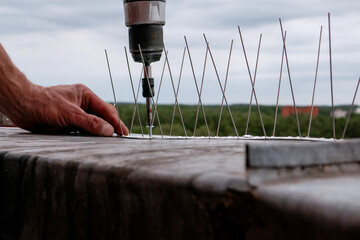 Close-up of a worker using a cordless power drill to install stainless steel bird deterrent spikes...