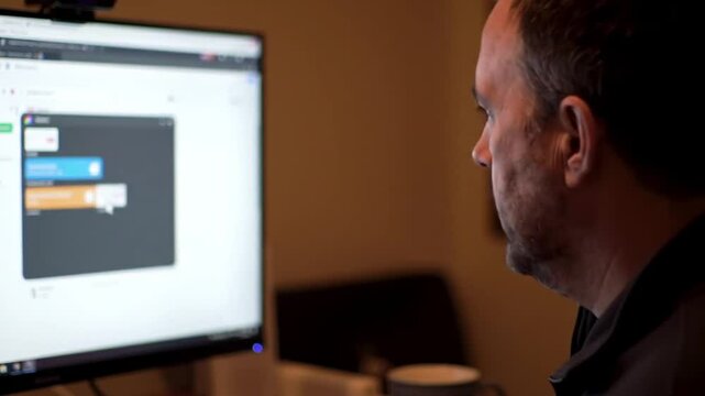 Man designing webpage on computer. Suitable for technology, web design, coding, or freelance work concepts. Creative workspace. Technology industry.