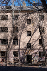 Old abandoned apartment building with shattered windows and damaged brickwork, surrounded by bare...