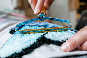 Close-up of a person using a rug carving tool on a tufted rug, detailing the finishing process in...