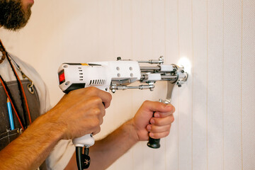 Close-up of a hand-held tufting gun being used to create a rug with green yarn, showing detail of...