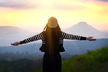 Silhouette of young woman standing on top of mountain and looking at sunrise