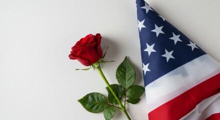 A red rose placed gently beside a folded U.S. flag, photographed on an isolated white background.