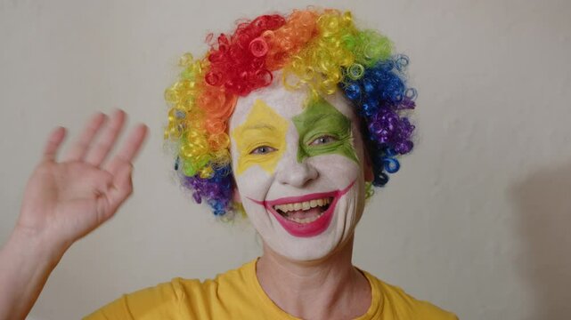 Smiling clown waving hand in greeting while looking at camera.