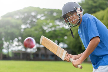 A teenage boy wearing a blue shirt and helmet holding a cricket bat, playing and hitting cricket ball on a school field. He looks focused and ready for action, in motion, selective focus on boy.