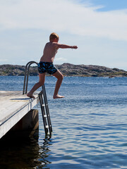 A young boy jumping from a pier in to the water a clear sunny summer day