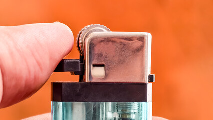 Finger activating a metallic lighter with an orange backdrop creating a warm contrast