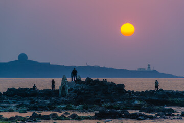 Visitors enjoy a magnificent sunset over the Shimen coastline in New Taipei City, Taiwan, with the...