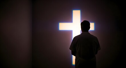 A person stands in silhouette, facing a glowing cross on a wall.