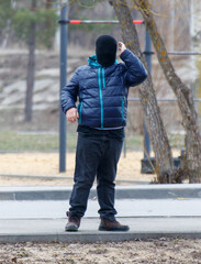 A man in a black hoodie and mask stands on a sidewalk
