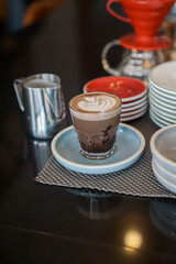 A glass of layered beverage topped with intricate froth art featuring a heart design