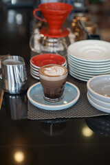 A glass of layered latte topped with intricate froth art featuring a heart design