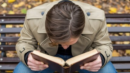 Young caucasian adult male reading book on park bench in autumn