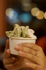 Hand holding a cup of ice cream with two scoops, one green and one white