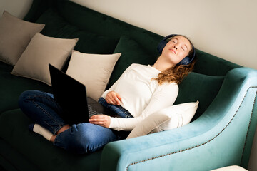 Young woman resting on green sofa during remote online work or distance study in living room at...