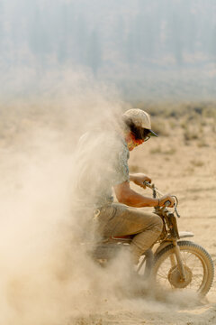 Motorcyclist riding on dirt road kicking up dust cloud