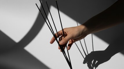 Female hand holding incense sticks casting shadows on minimalist background