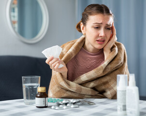 Sick woman with plaid on her shoulders suffers from a runny nose