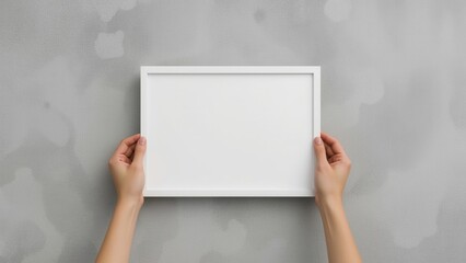 Hands holding an empty white frame against a grey wall, inviting personalization and creative expression.