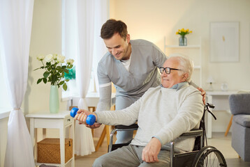 Disabled senior patient in a wheelchair performing stretching exercises with a dumbbell, assisted...