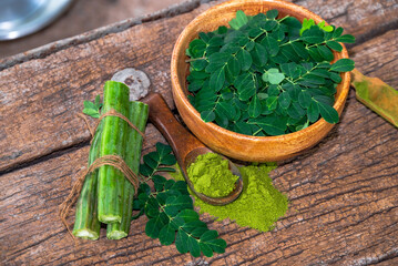 Moringa leaves in wooden bowl with Moringa powder on wooden background