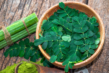 Moringa leaves in wooden bowl with Moringa powder on wooden background