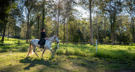 sideshot of a woman riding a white horse in the forest