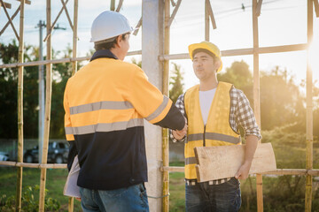 An elderly engineer and a middle-aged man shake hands at a construction site, symbolizing mutual...