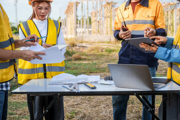 At a table on a construction site, an elderly male safety expert, a middle-aged man, and two young...